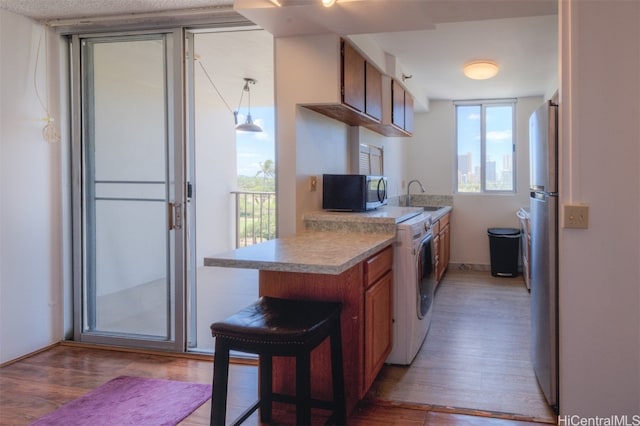 kitchen featuring appliances with stainless steel finishes, light hardwood / wood-style flooring, decorative light fixtures, and kitchen peninsula