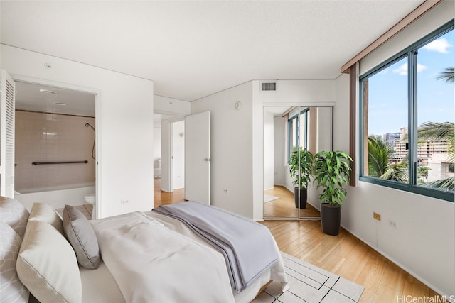 bedroom with connected bathroom, light hardwood / wood-style floors, and a closet