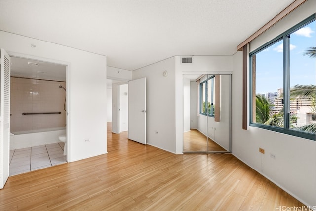 unfurnished bedroom with a closet, ensuite bathroom, a textured ceiling, and light hardwood / wood-style flooring