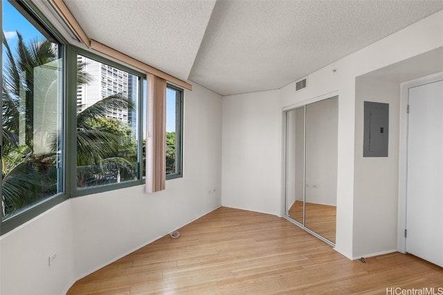 unfurnished bedroom featuring light hardwood / wood-style floors, a closet, a textured ceiling, and electric panel