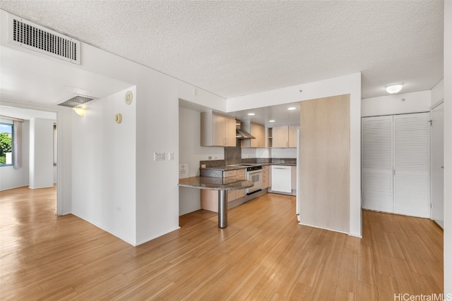 kitchen featuring dishwasher, a textured ceiling, wall chimney exhaust hood, range with electric stovetop, and light hardwood / wood-style flooring