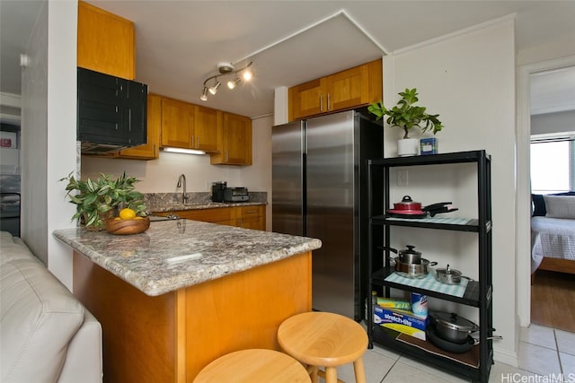 kitchen with kitchen peninsula, stainless steel fridge, light tile patterned floors, and light stone counters