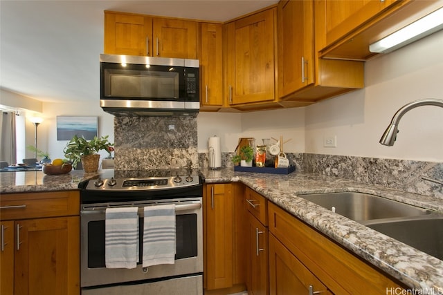 kitchen with decorative backsplash, stone counters, sink, and stainless steel appliances