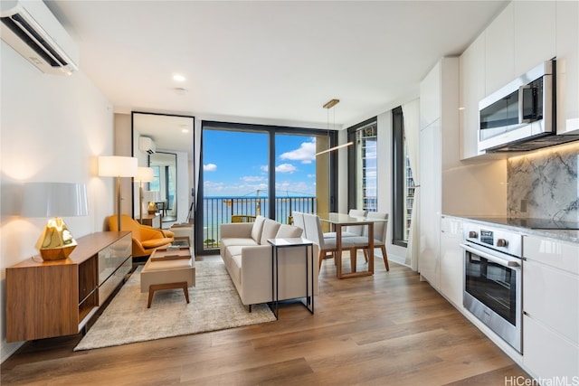 living room with a wall unit AC, wood finished floors, and floor to ceiling windows