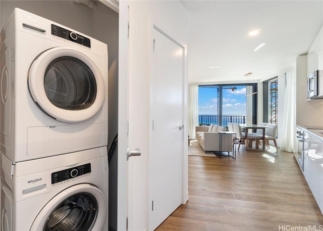 clothes washing area with laundry area, recessed lighting, stacked washer and clothes dryer, and light wood-style floors