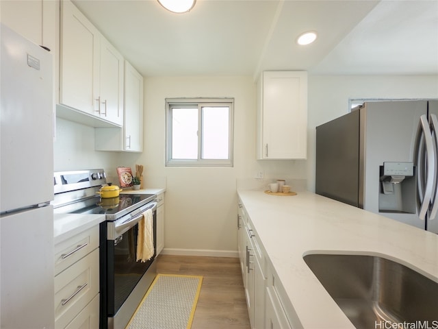 kitchen featuring appliances with stainless steel finishes, white cabinetry, light stone countertops, light hardwood / wood-style flooring, and sink