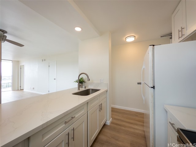 kitchen with white cabinetry, white fridge, sink, and light stone counters