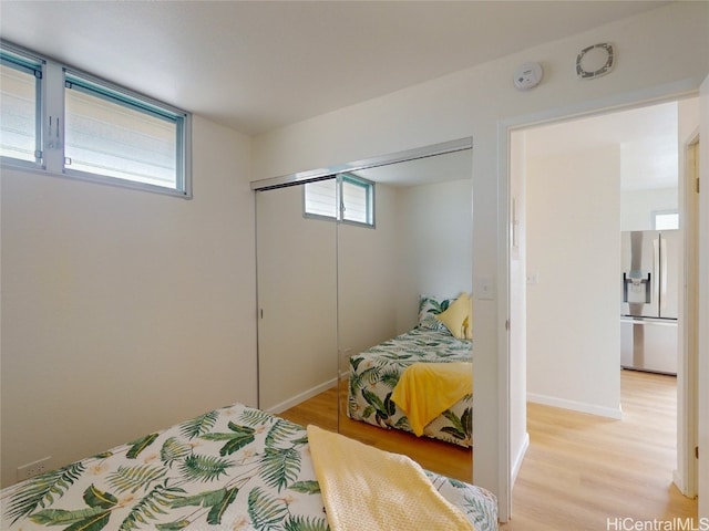 bedroom with a closet, stainless steel fridge, and light wood-type flooring