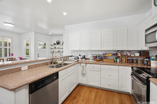 kitchen with appliances with stainless steel finishes, sink, white cabinets, light stone counters, and light wood-type flooring