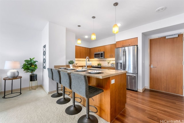 kitchen with kitchen peninsula, stainless steel appliances, dark wood-type flooring, hanging light fixtures, and a breakfast bar area