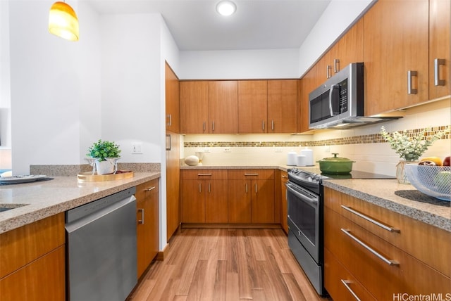 kitchen with decorative backsplash, light stone countertops, stainless steel appliances, and light hardwood / wood-style flooring