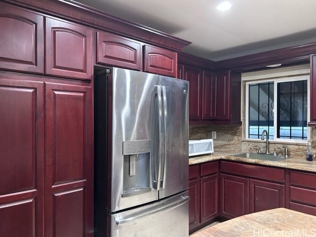 kitchen featuring light stone countertops, sink, decorative backsplash, and stainless steel refrigerator with ice dispenser