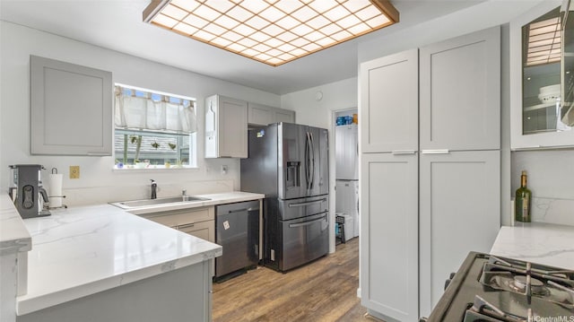 kitchen featuring appliances with stainless steel finishes, light stone countertops, light wood-type flooring, a sink, and gray cabinetry