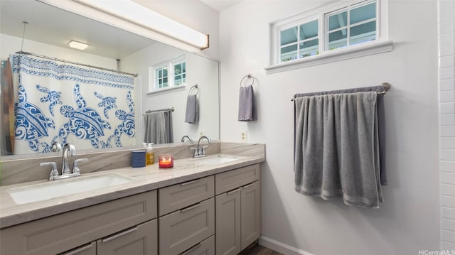 full bath featuring a shower with shower curtain, double vanity, baseboards, and a sink