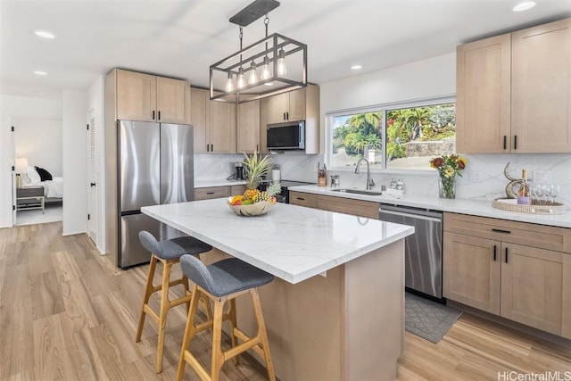 kitchen with sink, light hardwood / wood-style flooring, decorative light fixtures, a kitchen island, and stainless steel appliances