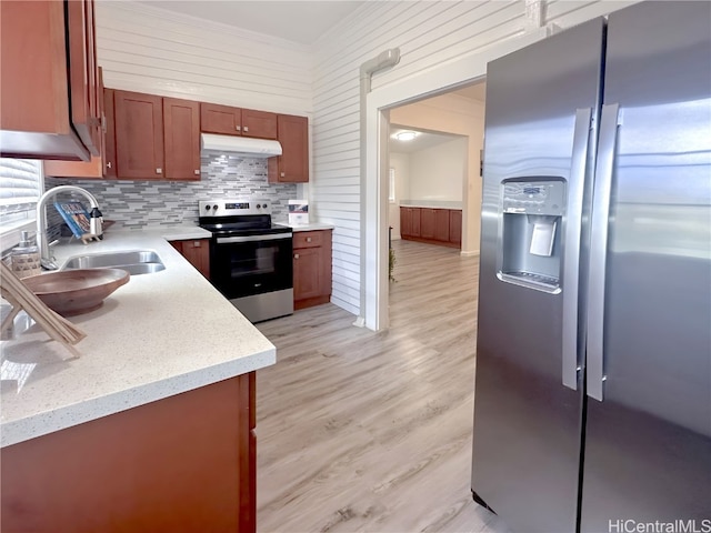 kitchen featuring decorative backsplash, wooden walls, stainless steel appliances, sink, and light wood-type flooring