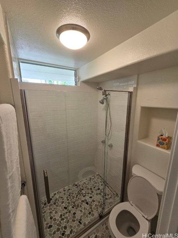 bathroom featuring toilet, a textured ceiling, a shower with shower door, and a wealth of natural light