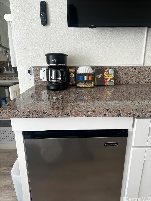 room details with hardwood / wood-style flooring, kitchen peninsula, dark stone countertops, stainless steel dishwasher, and white cabinetry