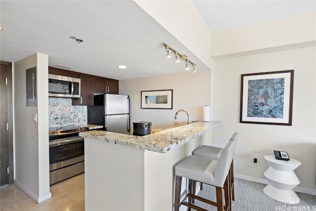 kitchen featuring decorative backsplash, a kitchen breakfast bar, kitchen peninsula, stainless steel appliances, and light stone counters