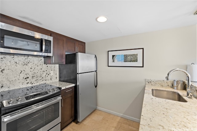 kitchen with light stone countertops, appliances with stainless steel finishes, sink, backsplash, and dark brown cabinetry