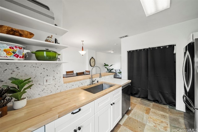 kitchen featuring stainless steel refrigerator, sink, black dishwasher, wood counters, and decorative light fixtures