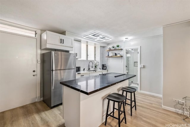 kitchen with stainless steel refrigerator, sink, a breakfast bar, white cabinets, and light wood-type flooring