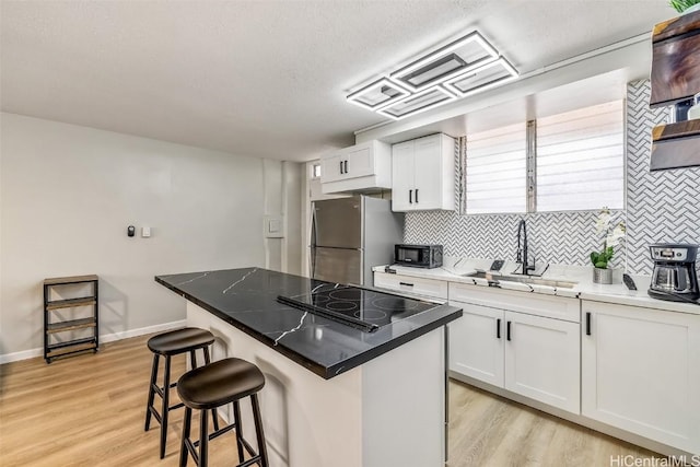 kitchen featuring black electric cooktop, tasteful backsplash, a breakfast bar area, a sink, and freestanding refrigerator