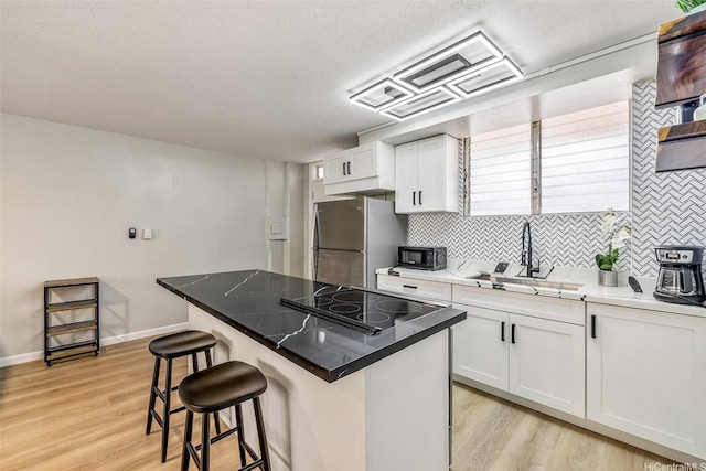 225 Liliuokalani Ave Unit 5C, Honolulu, HI 96815 - kitchen featuring freestanding refrigerator, a kitchen breakfast bar, decorative backsplash, light wood-style floors, and white cabinetry
