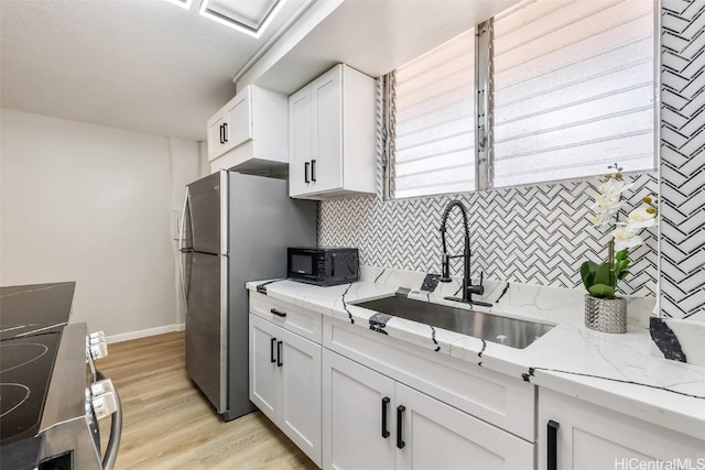 kitchen with white cabinets, sink, light stone countertops, light hardwood / wood-style floors, and range