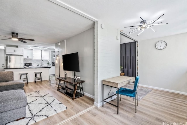 living area featuring baseboards, light wood-style floors, and ceiling fan