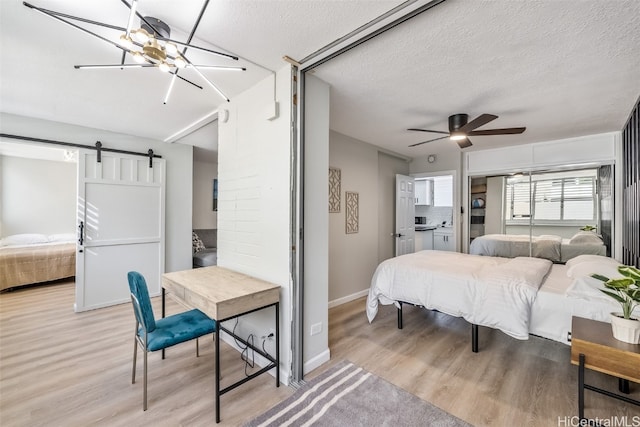 bedroom with a barn door, light hardwood / wood-style flooring, ensuite bathroom, a textured ceiling, and ceiling fan with notable chandelier