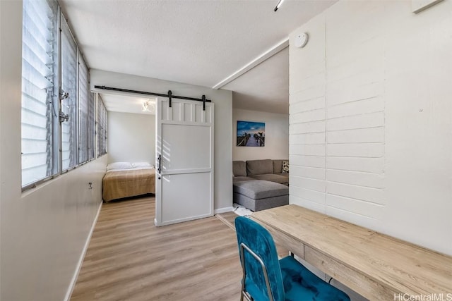 office area with baseboards, a barn door, wood finished floors, and a textured ceiling