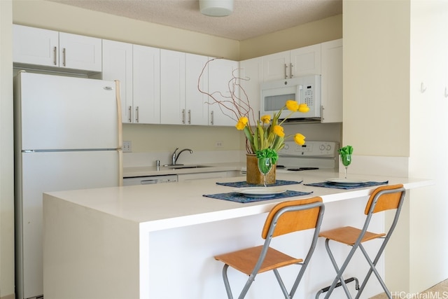 kitchen featuring a kitchen breakfast bar, kitchen peninsula, white cabinetry, and white appliances