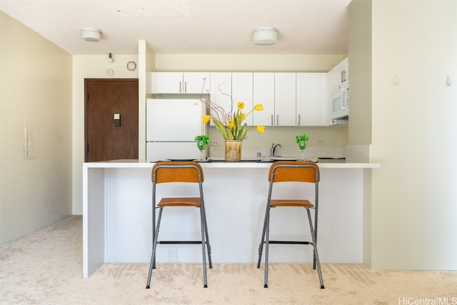 kitchen featuring a breakfast bar, white appliances, white cabinetry, and a peninsula