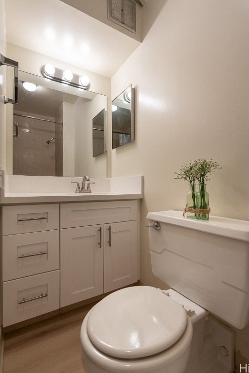 bathroom featuring visible vents, toilet, vanity, wood finished floors, and tiled shower