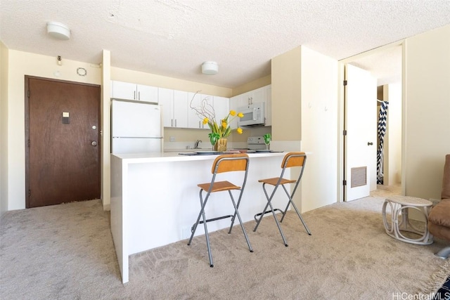 kitchen featuring visible vents, light colored carpet, white cabinets, white appliances, and a peninsula