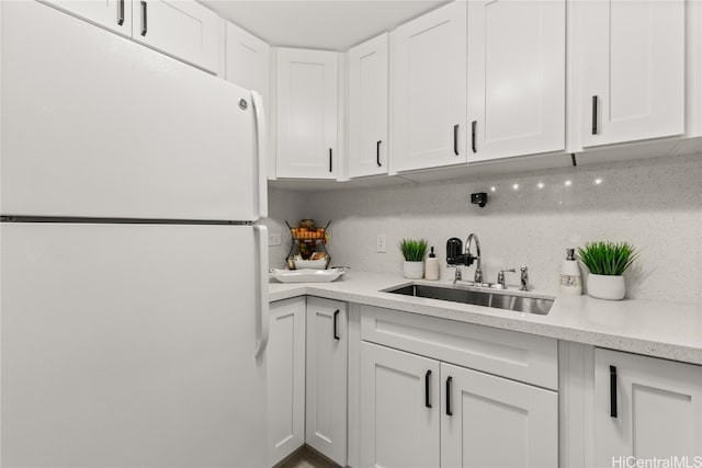 kitchen featuring white refrigerator, backsplash, white cabinetry, and sink