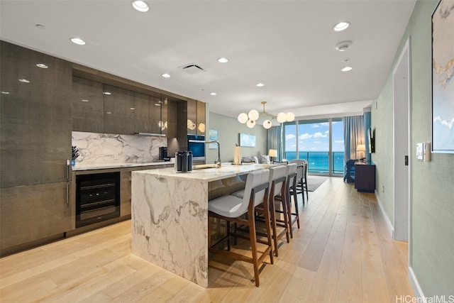 kitchen with light wood-type flooring, beverage cooler, a water view, a breakfast bar area, and a kitchen island with sink