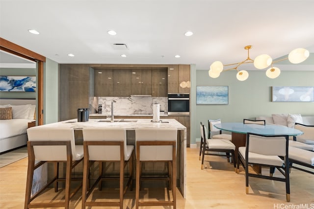 kitchen featuring oven, a breakfast bar, decorative light fixtures, light hardwood / wood-style floors, and tasteful backsplash