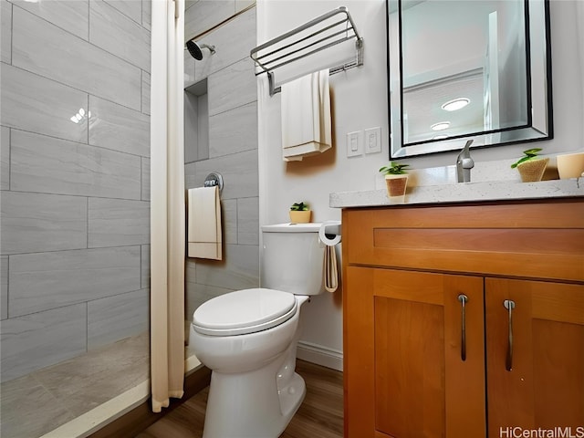 bathroom featuring toilet, a tile shower, vanity, and wood-type flooring