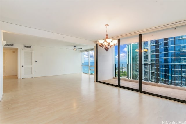 unfurnished room with expansive windows, hardwood / wood-style flooring, and ceiling fan with notable chandelier