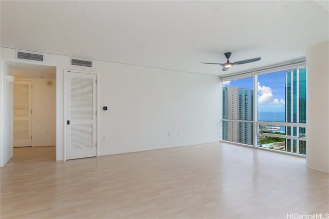 unfurnished room featuring a wall of windows, light wood-type flooring, and ceiling fan