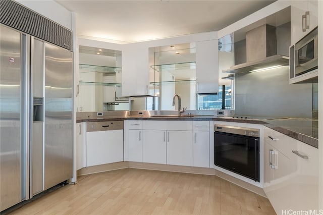 kitchen with wall chimney exhaust hood, built in appliances, sink, light wood-type flooring, and white cabinets