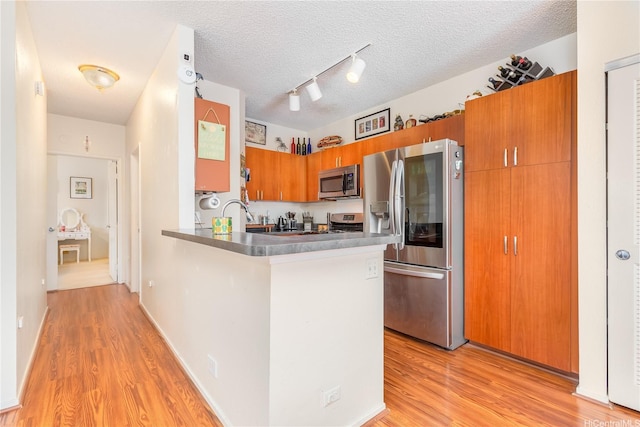 91-940 Puahala St Unit 39T, Ewa Beach, HI 96706 - kitchen with brown cabinetry, track lighting, a peninsula, light wood-type flooring, and stainless steel appliances