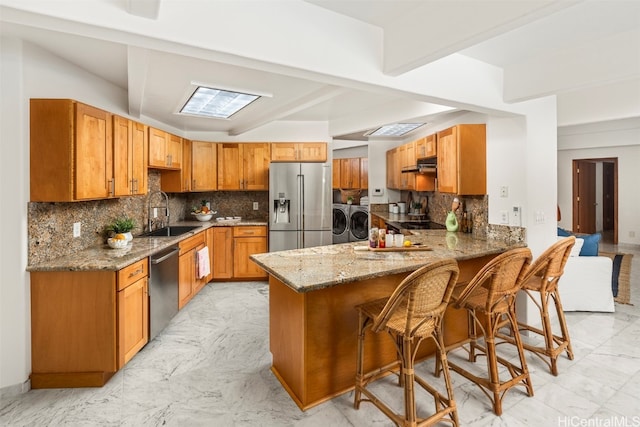 kitchen with decorative backsplash, a kitchen breakfast bar, kitchen peninsula, stainless steel appliances, and washer and dryer