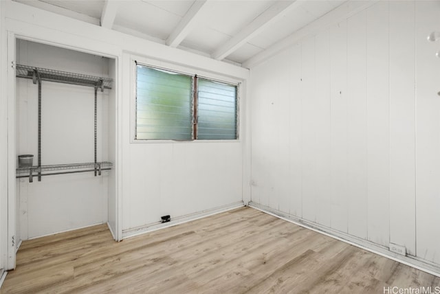 unfurnished bedroom with beamed ceiling, a closet, light hardwood / wood-style floors, and wood walls