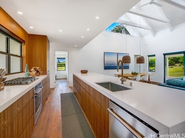 kitchen with appliances with stainless steel finishes, sink, hardwood / wood-style floors, hanging light fixtures, and beam ceiling