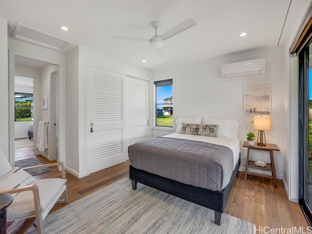 bedroom featuring multiple windows, hardwood / wood-style floors, an AC wall unit, and ceiling fan