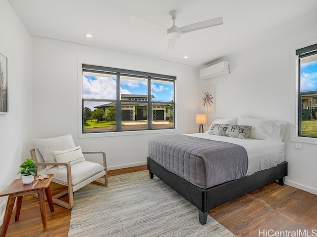 bedroom with a wall mounted AC, multiple windows, and hardwood / wood-style floors