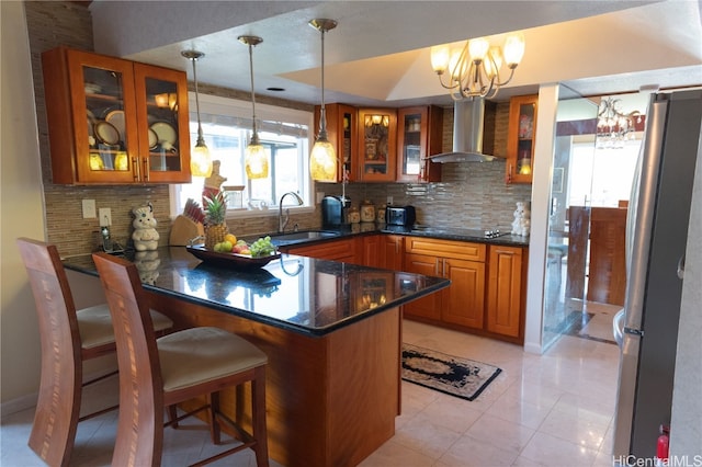 kitchen with hanging light fixtures, a breakfast bar area, stainless steel refrigerator, wall chimney exhaust hood, and sink